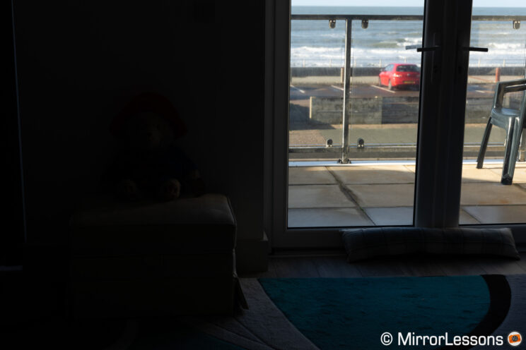 Dark leaving room with large window and sunshine outside