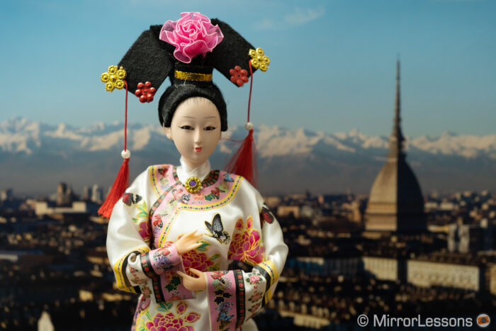 Japanese doll in front of the photo of a city panorama in the background. The image is brighter than the previous one.