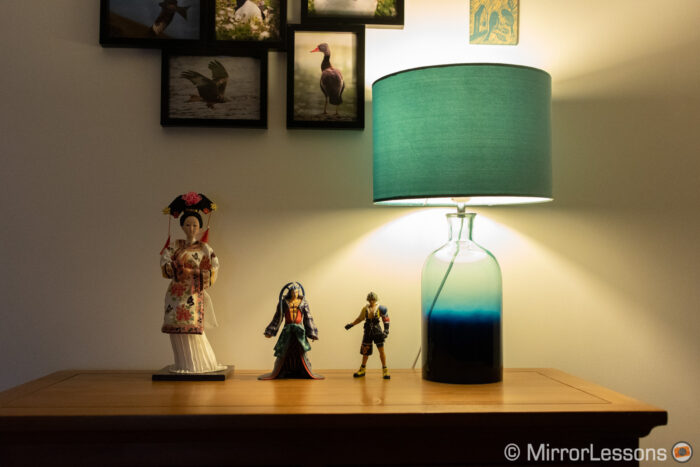 one japanese doll and two final fantasy action figures next to a lamp, on a chest of drawer. The image is correctly exposed.